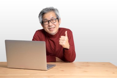 Beyaz arka planda, masada oturan kıdemli Asyalı adam..