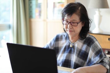 Dizüstü bilgisayar kullanan yaşlı Asyalı kadın..