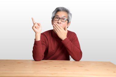 Beyaz arka planda, masada oturan kıdemli Asyalı adam..