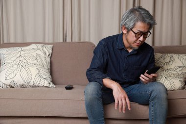 Oturma odasındaki kanepede oturan kıdemli Asyalı adam..