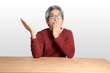 Beyaz arka planda, masada oturan kıdemli Asyalı adam..