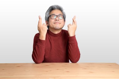 Beyaz arka planda, masada oturan kıdemli Asyalı adam..