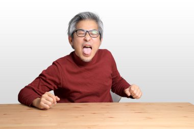 Beyaz arka planda, masada oturan kıdemli Asyalı adam..