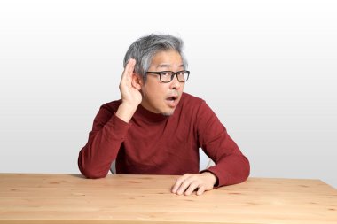 Beyaz arka planda, masada oturan kıdemli Asyalı adam..