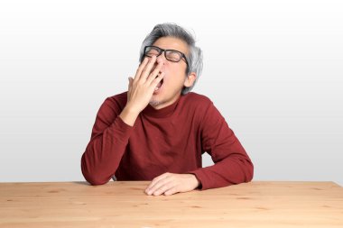 Beyaz arka planda, masada oturan kıdemli Asyalı adam..