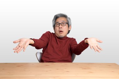 Beyaz arka planda, masada oturan kıdemli Asyalı adam..