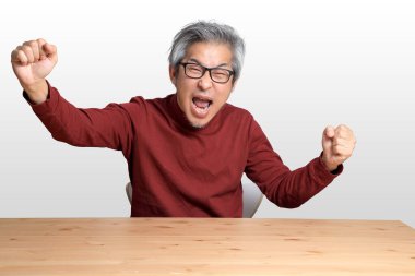 Beyaz arka planda, masada oturan kıdemli Asyalı adam..