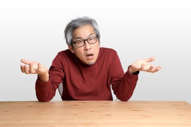 Beyaz arka planda, masada oturan kıdemli Asyalı adam..