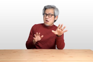 Beyaz arka planda, masada oturan kıdemli Asyalı adam..