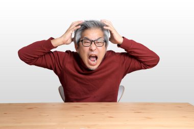 Beyaz arka planda, masada oturan kıdemli Asyalı adam..