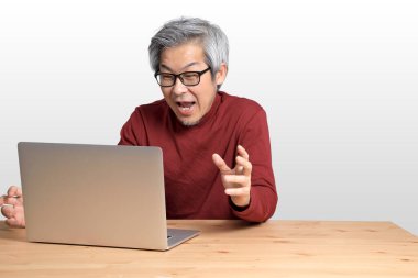 Beyaz arka planda, masada oturan kıdemli Asyalı adam..