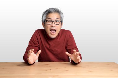 Beyaz arka planda, masada oturan kıdemli Asyalı adam..