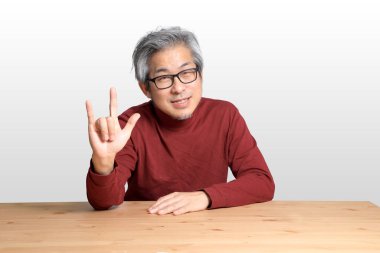 Beyaz arka planda, masada oturan kıdemli Asyalı adam..