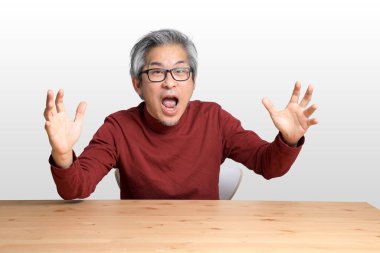 Beyaz arka planda, masada oturan kıdemli Asyalı adam..