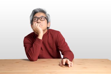 Beyaz arka planda, masada oturan kıdemli Asyalı adam..