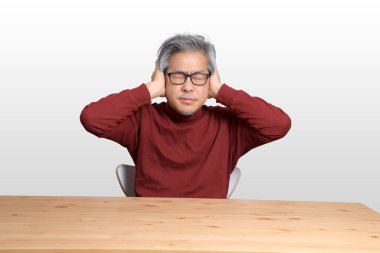 Beyaz arka planda, masada oturan kıdemli Asyalı adam..