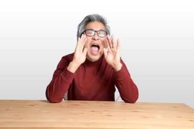 Beyaz arka planda, masada oturan kıdemli Asyalı adam..