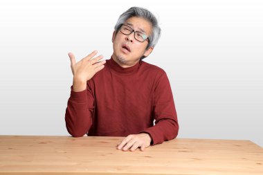 Beyaz arka planda, masada oturan kıdemli Asyalı adam..