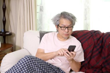 Oturma odasında akıllı telefon kullanan Asyalı adam..