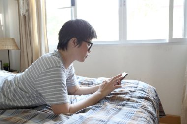 Yatakta akıllı telefon kullanan Asyalı kadın..