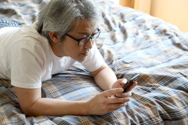 Yatakta akıllı telefon kullanan Asyalı adam..