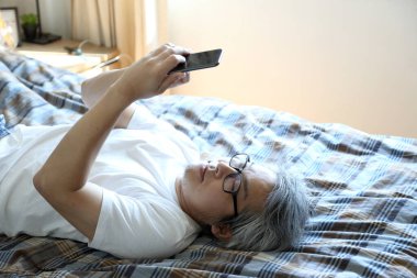 Yatakta akıllı telefon kullanan Asyalı adam..