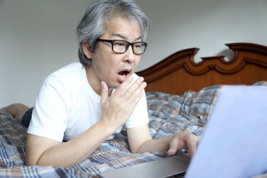 Yatakta dizüstü bilgisayar kullanan Asyalı adam..