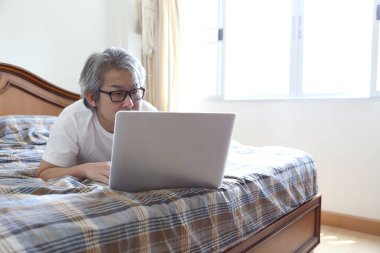 Yatakta dizüstü bilgisayar kullanan Asyalı adam..