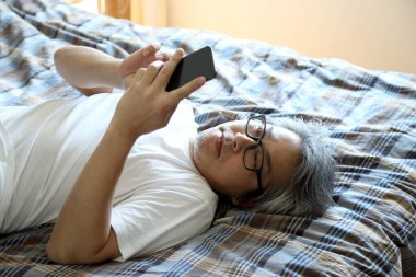 Yatakta akıllı telefon kullanan Asyalı adam..