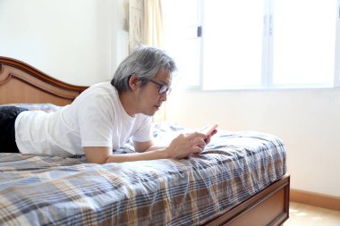 Yatakta akıllı telefon kullanan Asyalı adam..