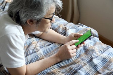 Yatakta akıllı telefon kullanan Asyalı adam..
