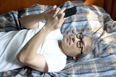 Yatakta akıllı telefon kullanan Asyalı adam..