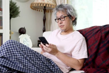 Oturma odasında akıllı telefon kullanan Asyalı adam..