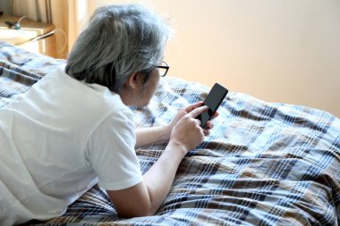 Yatakta akıllı telefon kullanan Asyalı adam..