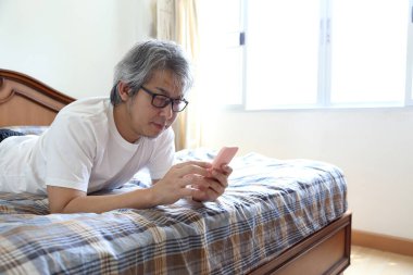 Yatakta akıllı telefon kullanan Asyalı adam..