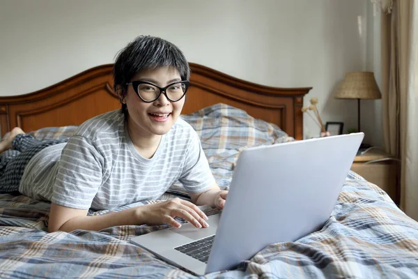 The Asian woman using laptop on the bed.