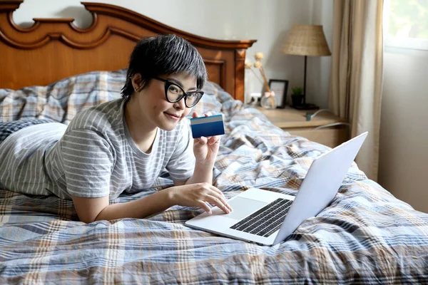 The Asian woman using laptop on the bed.