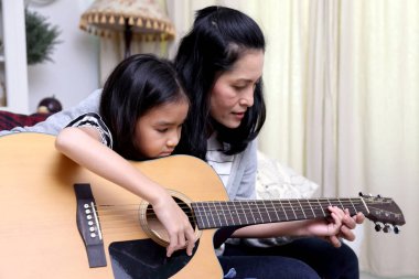 Asyalı anne çocuğuna gitar çalmayı öğretiyor..