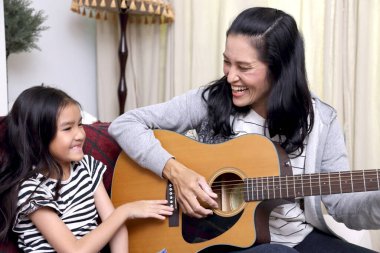 Asyalı anne çocuğuna gitar çalmayı öğretiyor..