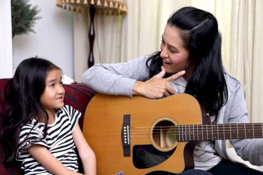 Asyalı anne çocuğuna gitar çalmayı öğretiyor..