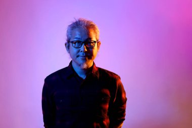 Beyaz arka planda jel renkli ışıkla poz veren Asyalı adam..