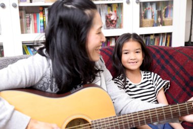 Asyalı anne çocuğuna gitar çalmayı öğretiyor..