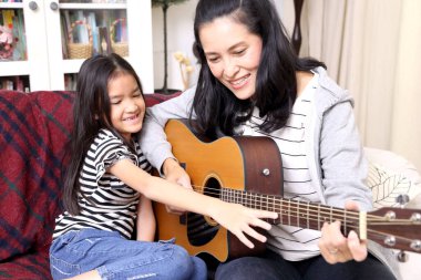 Asyalı anne çocuğuna gitar çalmayı öğretiyor..