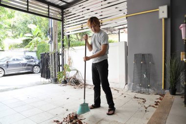 Güneydoğu Asyalı adam evin önündeki yaprakları temizleyip süpürüyor..