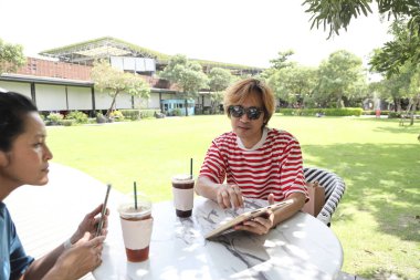 Güneydoğu Asyalı adam çalışmalarını dijital tablette gösteriyor ve bir açık kahve dükkanında arkadaşlarıyla konuşuyor..