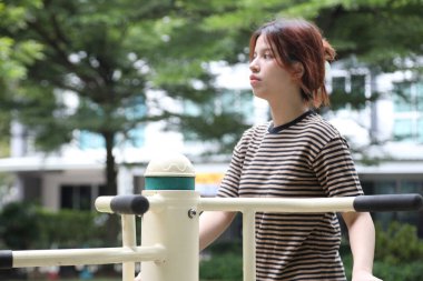 Güneydoğu Asyalı bir kadın parkta egzersiz makinesi kullanıyor.