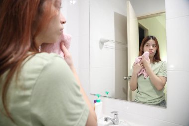 Güneydoğu Asyalı bir kadın lavaboda yüzünü havluyla yıkıyor..