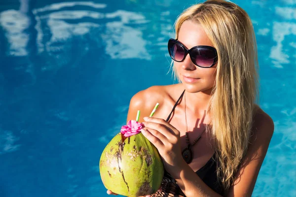 Unga vackra blonda kvinnan i poolen med kokos cocktail — Stockfoto