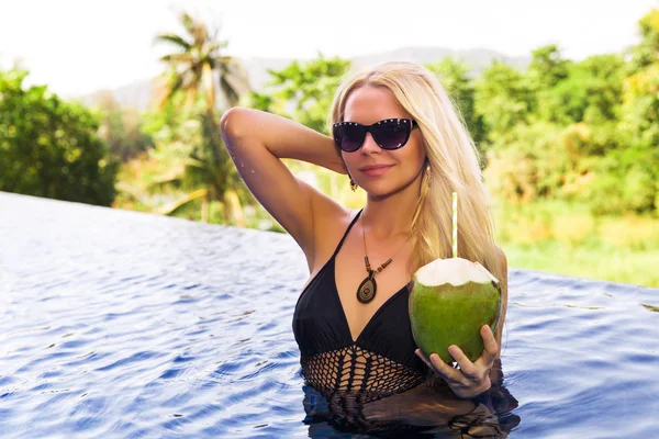 Junge hübsche blonde Frau im Schwimmbad mit Kokosnuss-Coctail — Stockfoto