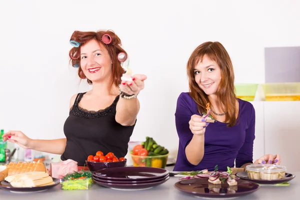 两个年轻漂亮的女人家庭主妇烹饪用睫毛夹头发 — 图库照片